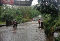 Kondisi banjir di Permu Bawah menyebabkan air meluber ke jembatan dan menghambat lalu lintas akibat saluran drainase tertutup sampah kasur dan pendangkalan karena sedimentasi